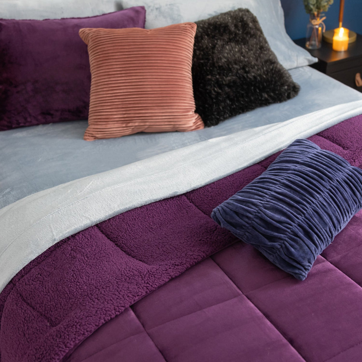 Image of a bed styled with light blue sheets and a purple comforter set