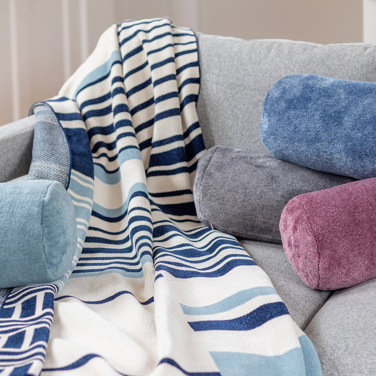 Image of a grey neck roll pillow placed on a pink and grain colored pair of extra-fluffy™ throws