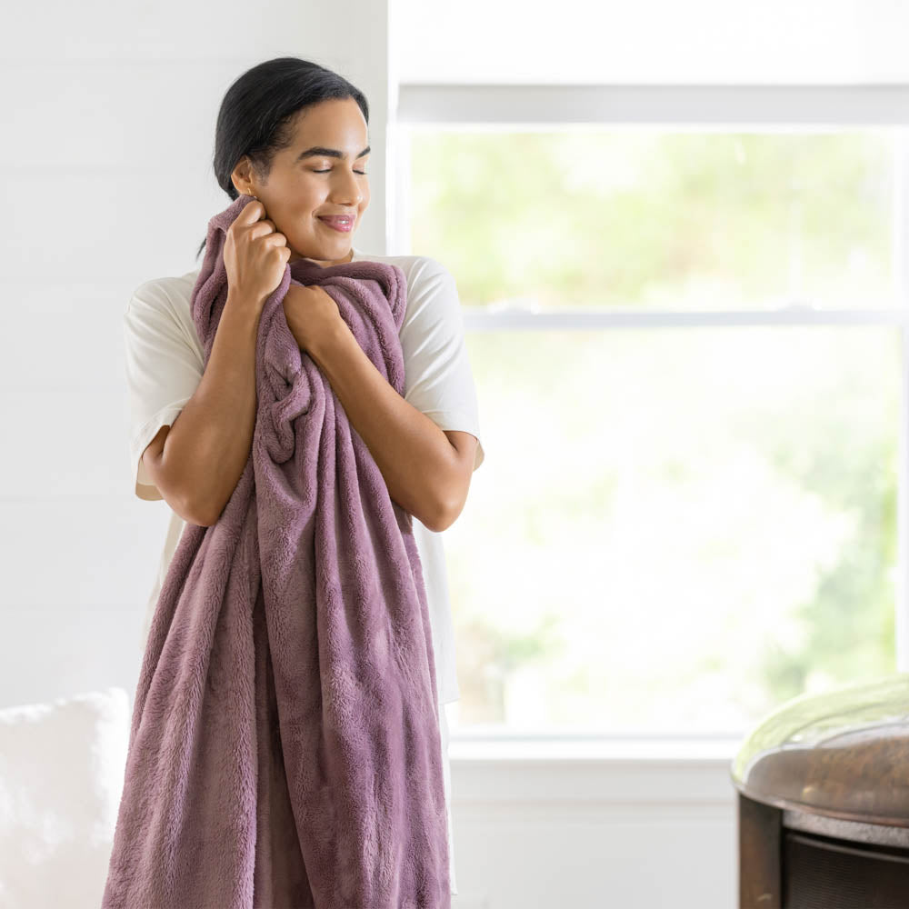 A woman standing in a white room holding a purple PrimaLush throw.
