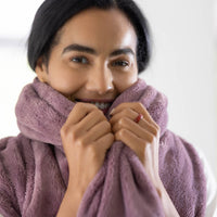 A woman smiling and snuggling her face in a purple PrimaLush throw.