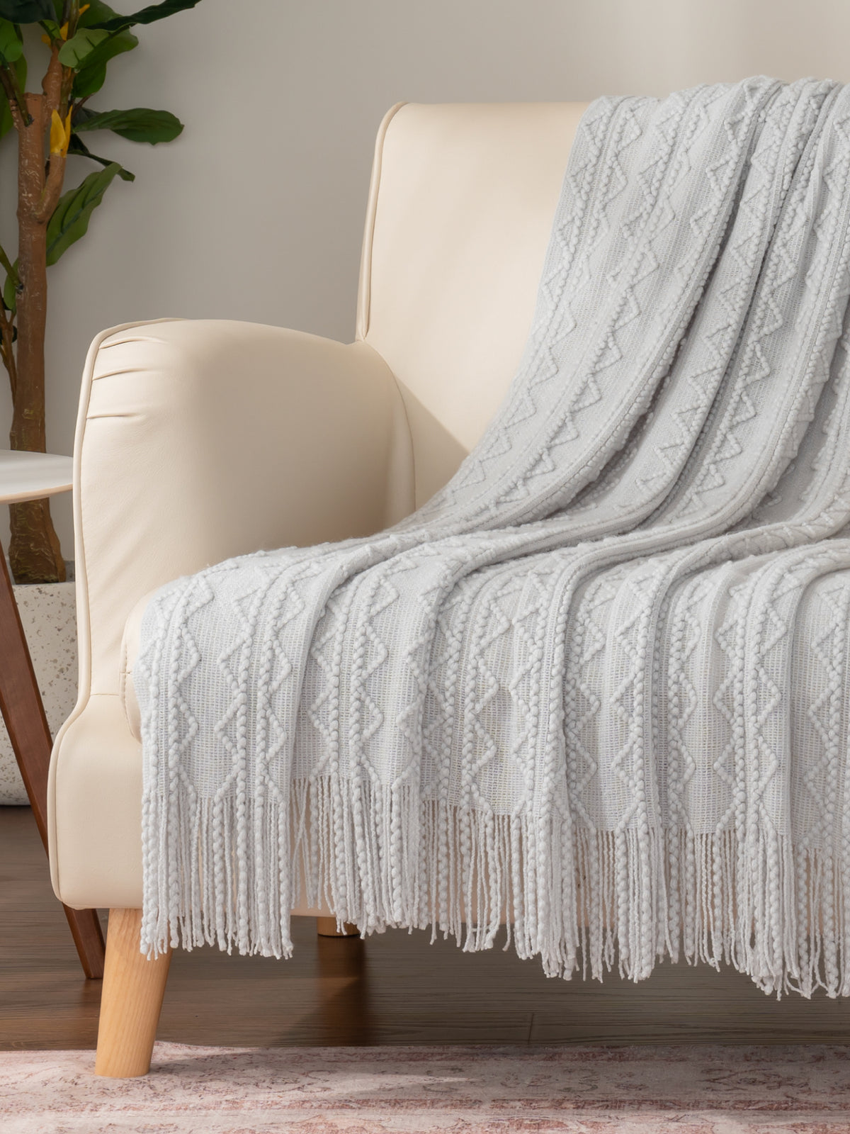New arrivals collection image featuring our Tassel Knit Throw in Grey draped over a beige leather chair.
