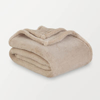 A tan extra-fluffy throw folded enatly on a white surface.