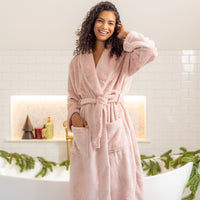 Woman wearing a pink robe in a bathroom setting with decorative elements.