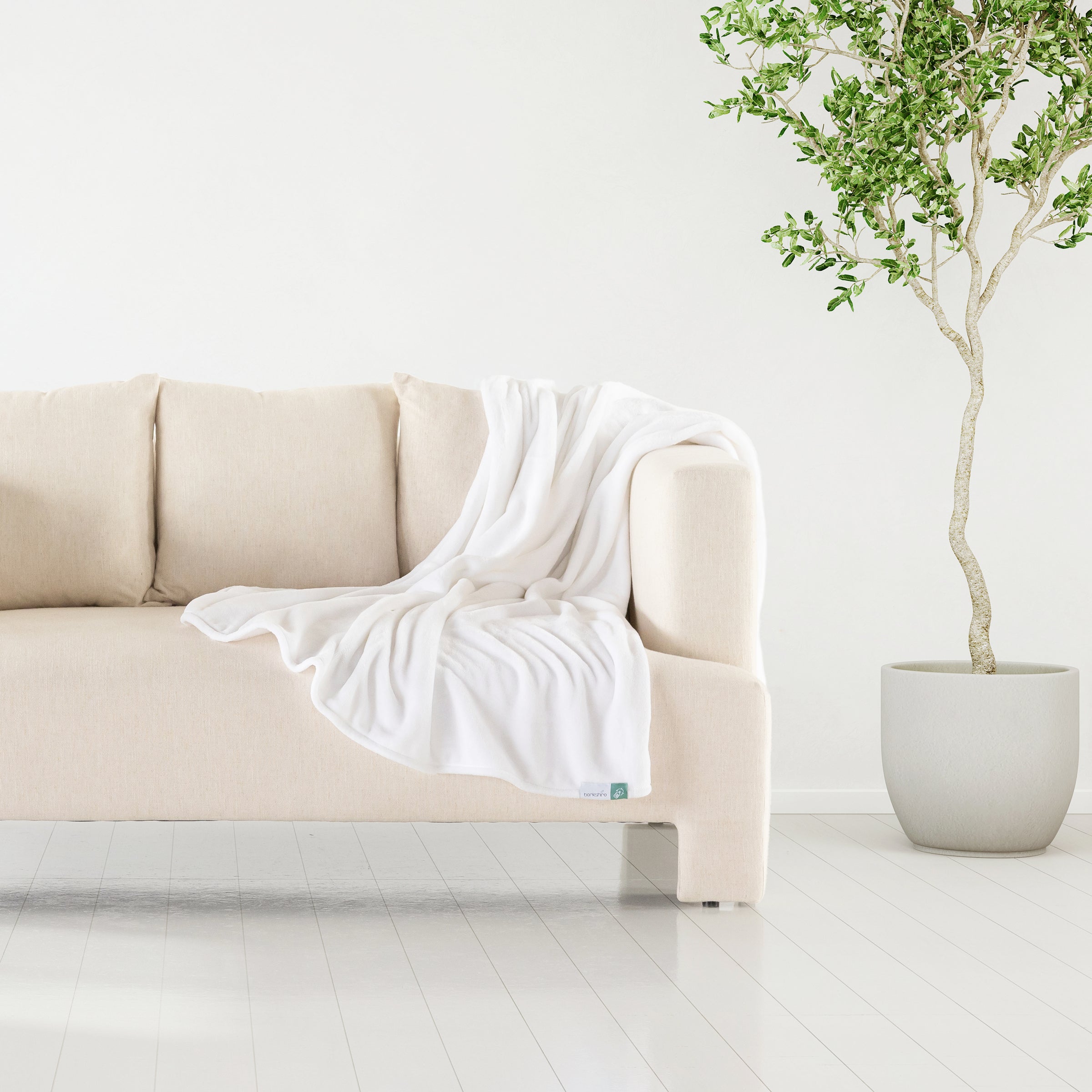 A white velvety plush throw draped over the arm of a beige sofa next to a plant.