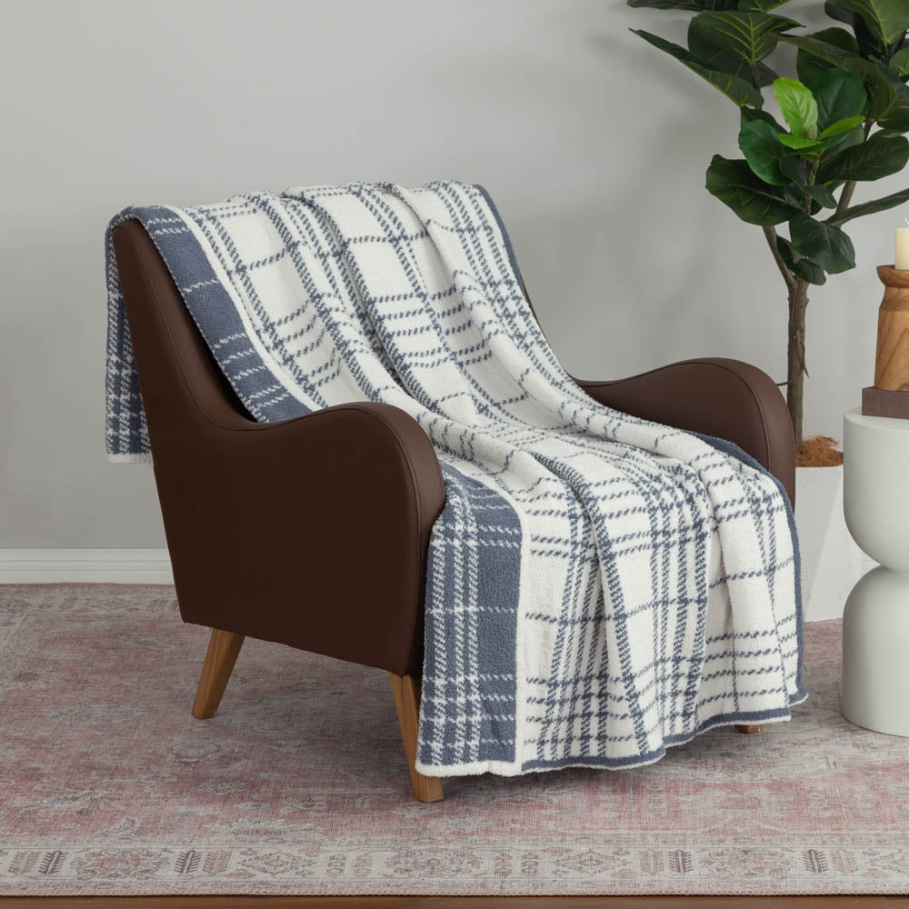 A white and blue plaid knitted throw draped neatly over a brown leather chair.