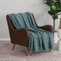 Dusk blue PrimaLush throw draped neatly over a brown leather chair next to a plant.