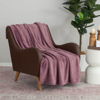 A purple PrimaLush throw draped neatly over a brown leather chair next to a plant and table.