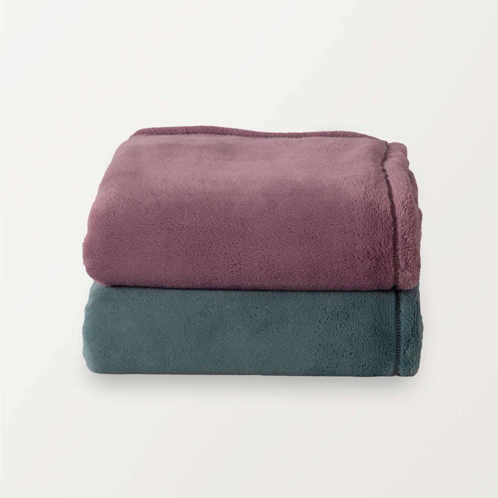 Purple and blue PrimaLush throws stacked neatly on a white surface.