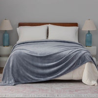A blue velvet blanket draped over a bed with white pillows and blue lamps.