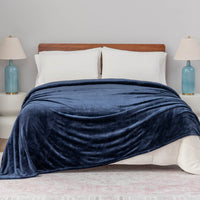A dark blue velvet blanket draped over a bed with white pillows and blue lamps.