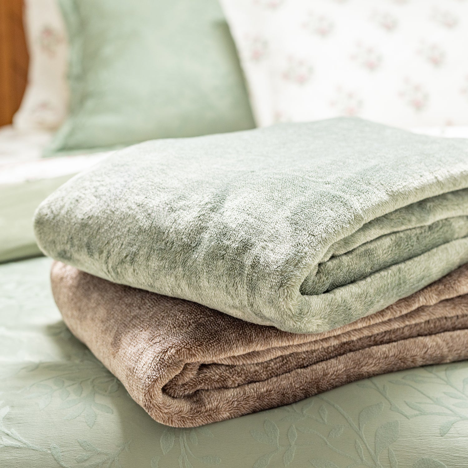 Folded green and brown blankets on a bed with a floral headboard.