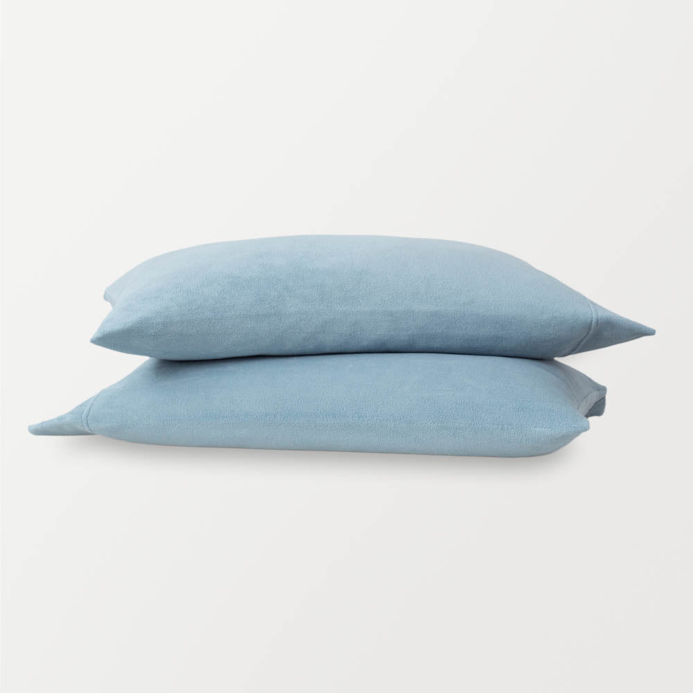 Blue pillowcases stacked ontop of eachother on a white surface.