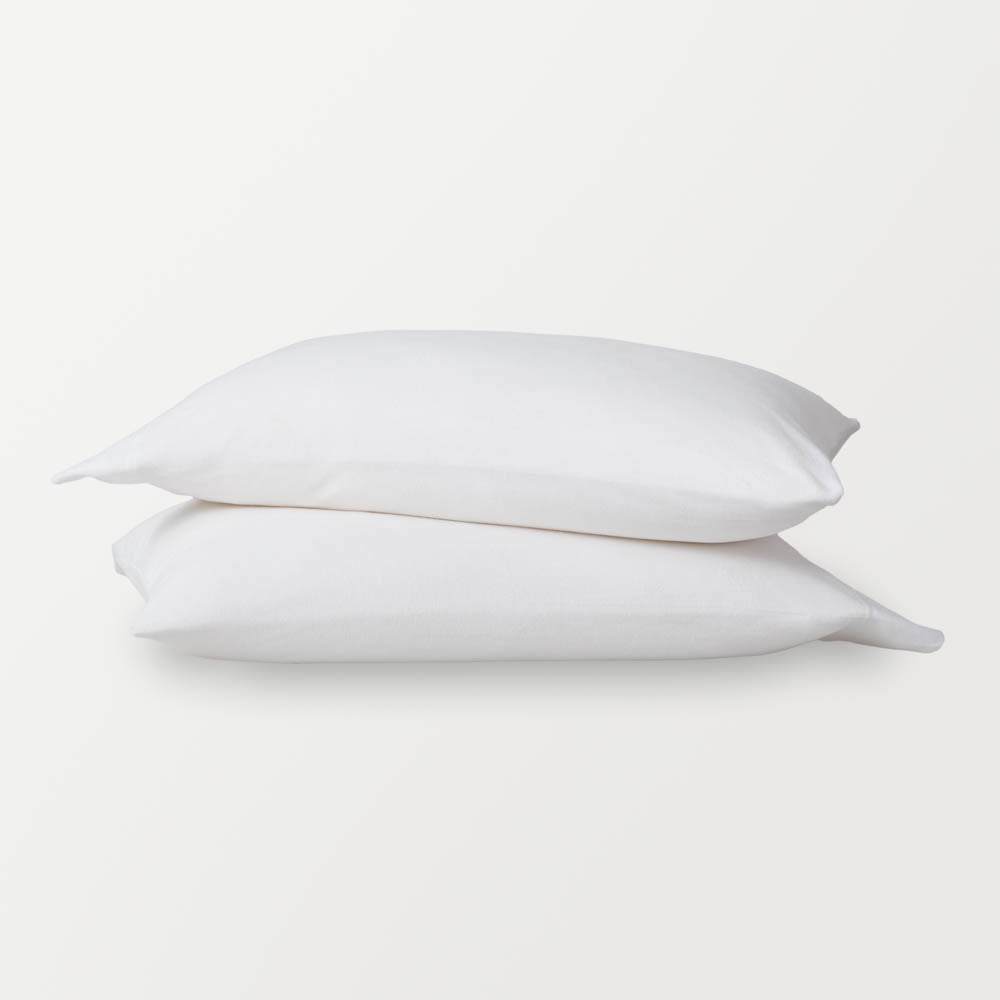 White pillowcases stacked ontop of eachother on a white surface.