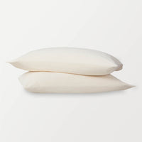 Warm ivory pillowcases stacked on top of eachother on a white surface.