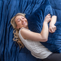 Close-up of a woman hugging a pillow laying on soft, plush Dress Blue sheet set and sherpa comforter set.
