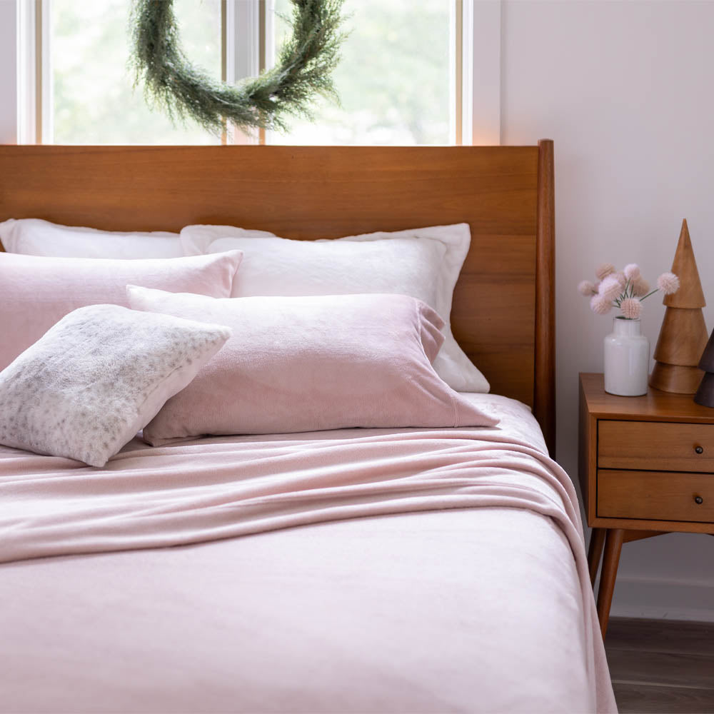 Rose Smoke Sheet (blush color) set on a wooden bed with decorative pillows and a holiday wreath in the background.
