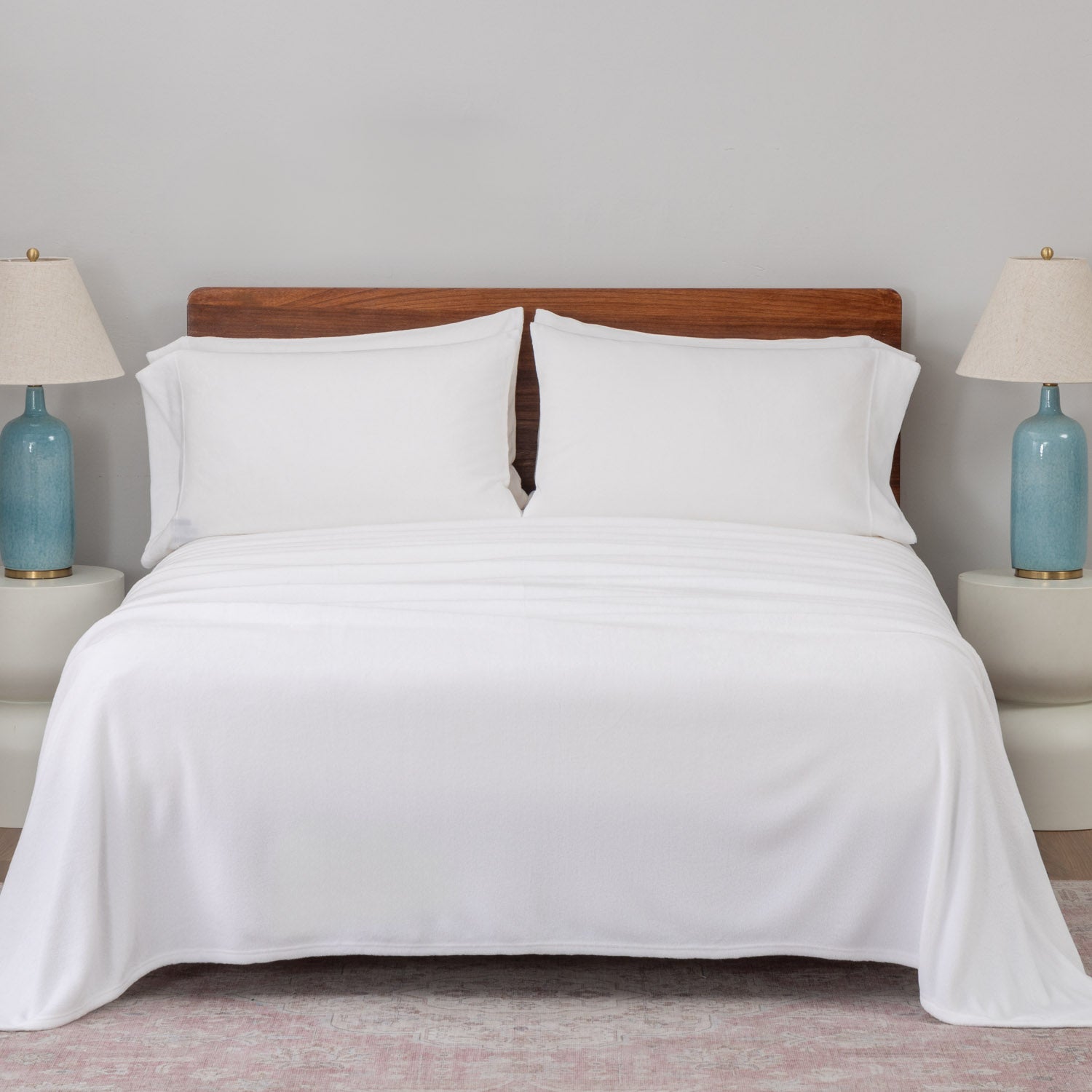 Bed with white bedding and wooden headboard in a room with two lamps on nightstands.