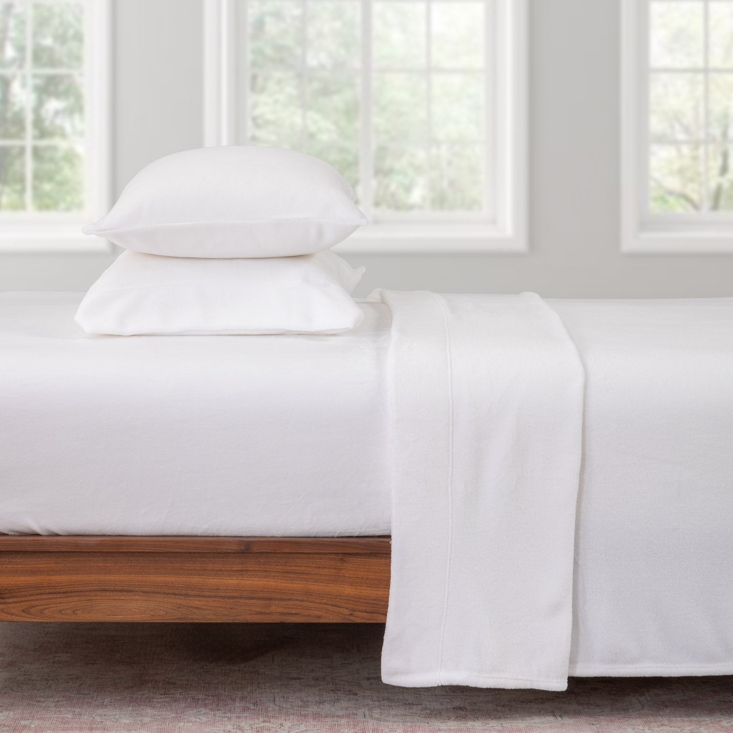 White bedding set on a wooden bed with large windows in the background