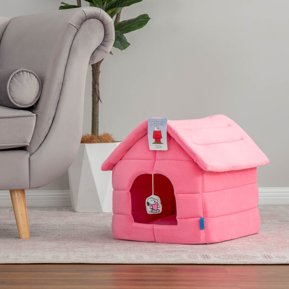 Our pink Peanuts Snoopy Dog House Pet Bed sitting next to a grey sofa in a living room.