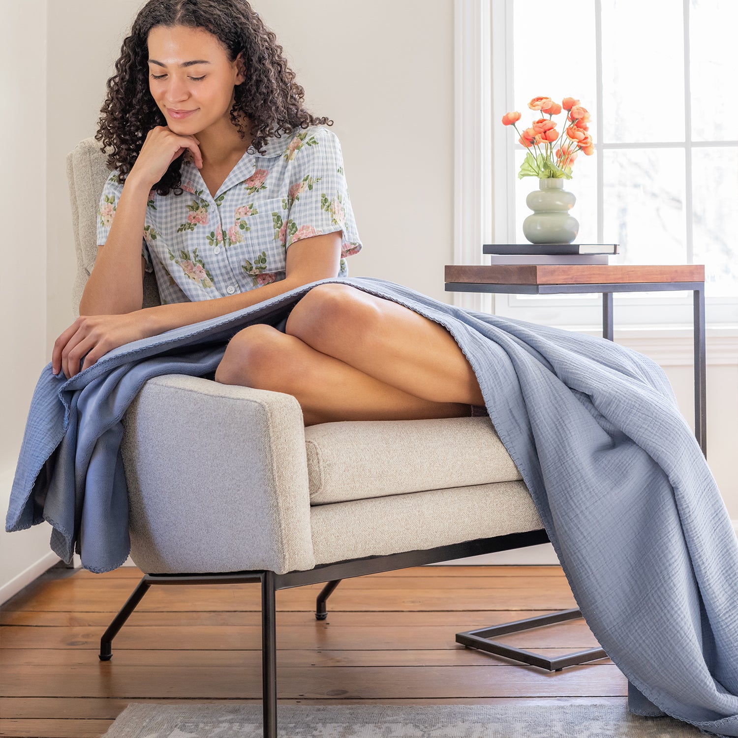 A woman sitting on a grey chair with a blue gauze throw draped over her legs.