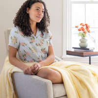 A woman sitting on a grey chair with a yellow throw draped over her legs.