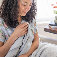 A woman holding a grey throw in her hands while smiling.
