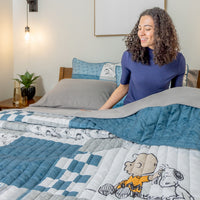 Woman arranging a quilt with cartoon characters on a bed in a bedroom setting.
