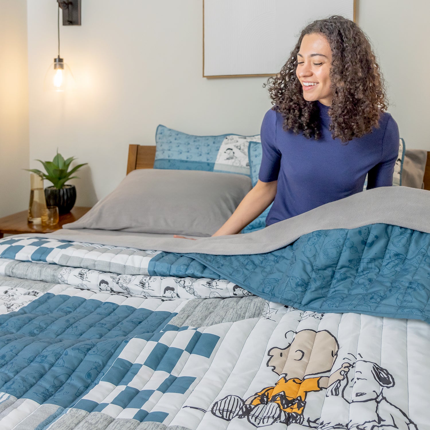 Woman arranging a quilt with cartoon characters on a bed in a bedroom setting.