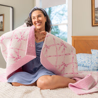 Woman wrapped in a pink and white blanket sitting on a bed.