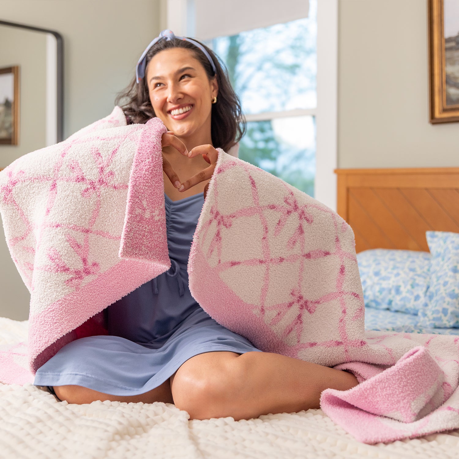 Woman wrapped in a pink and white blanket sitting on a bed.