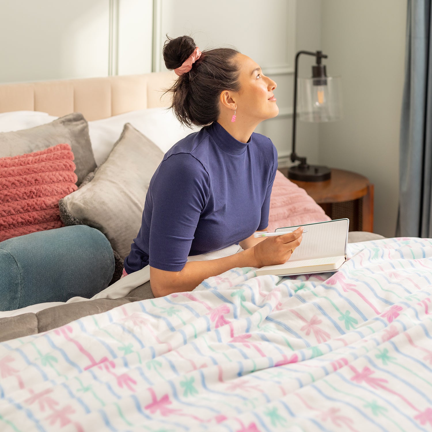Woman sitting on a bed holding a notebook in a bedroom setting.