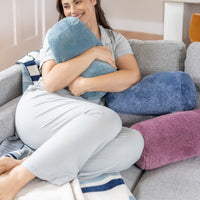 Woman sitting on a couch holding a blue pillow with more pillows in the background.