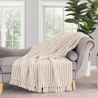 Beige woven throw blanket on a gray sofa in a living room setting with a plant in the background.