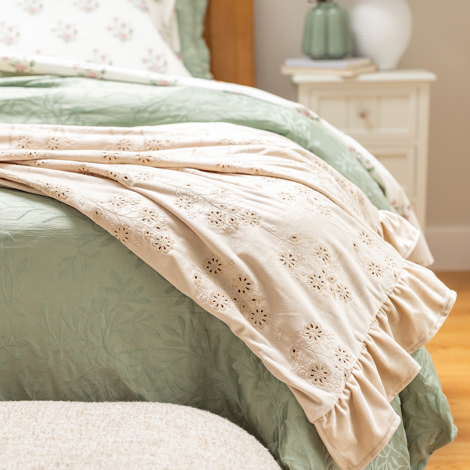 Neatly made bed with a beige embroidered blanket and green bedding in a bedroom setting.