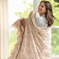 Woman wrapped in a beige floral-patterned blanket indoors with a window in the background