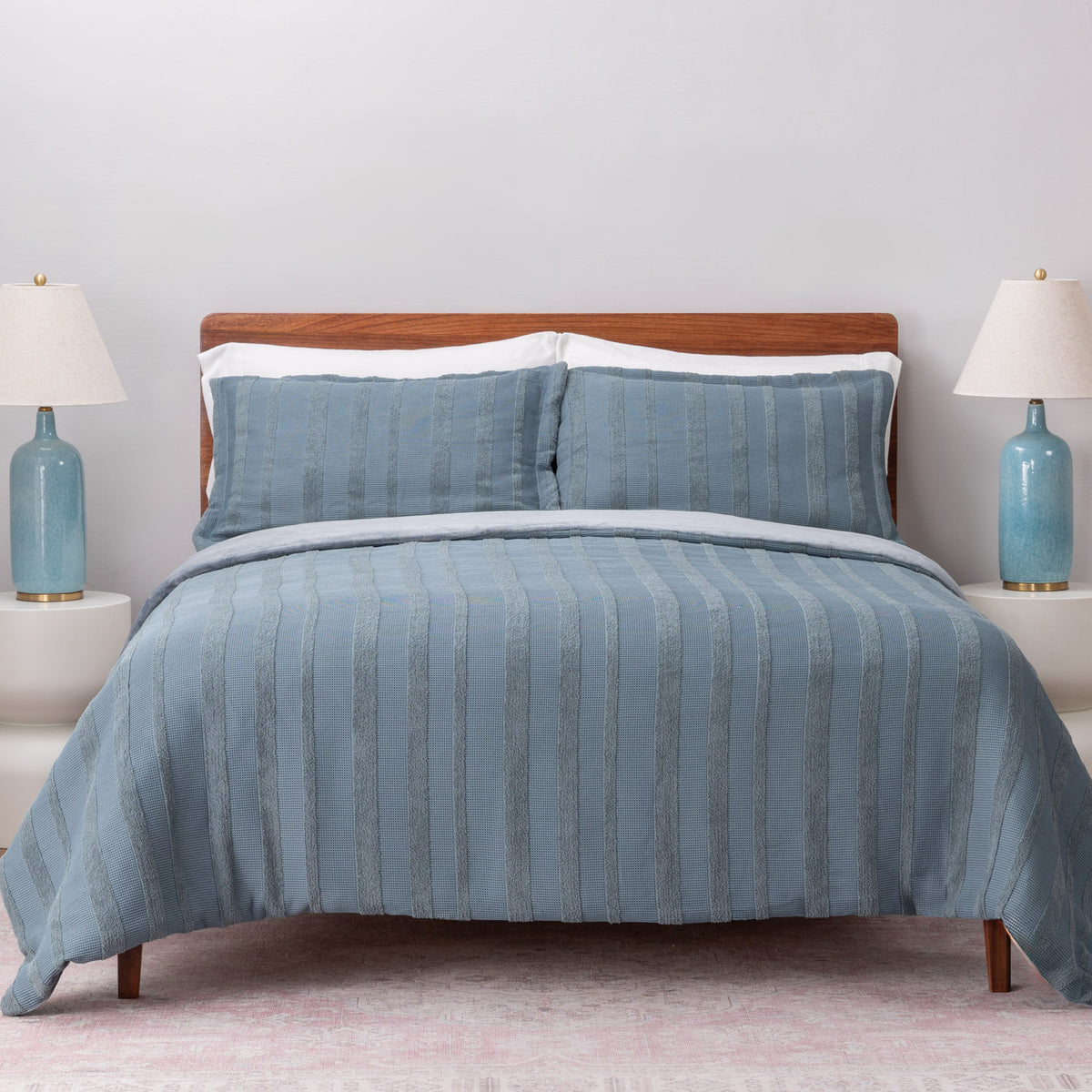 Blue striped bedding set on a bed with matching pillows and lamps in the background.