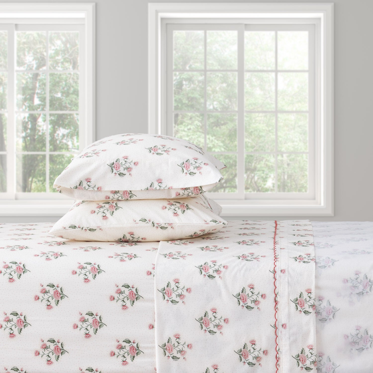 Floral bed sheet set on a bed with pillows in a room with windows.