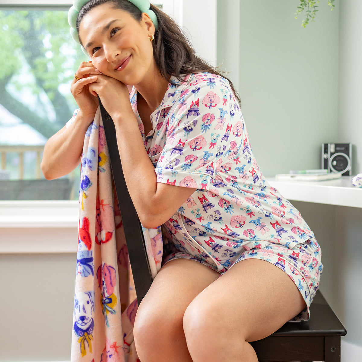 Woman in a colorful pajama set sitting on a chair with a throw blanket, smiling.