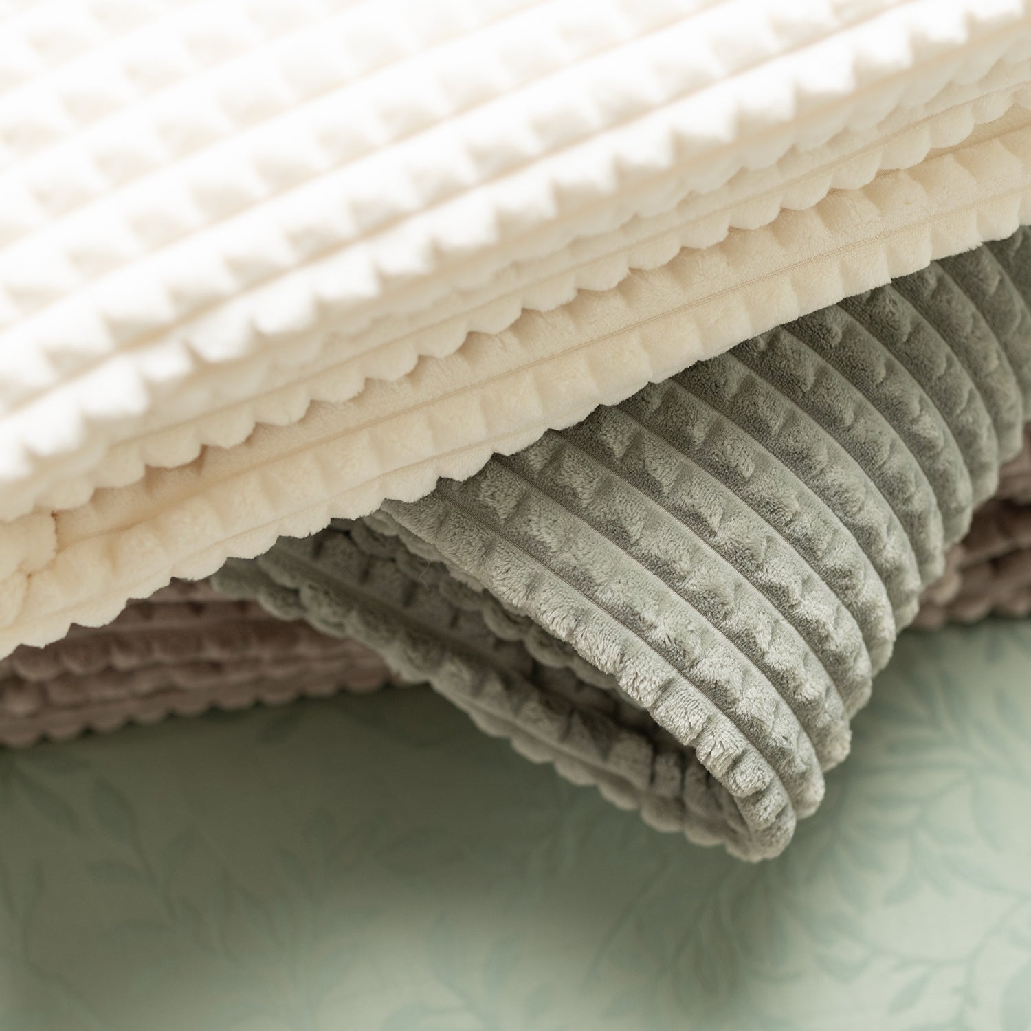 Stack of folded textured fabric swatches in beige, gray, and pink on a light green background.