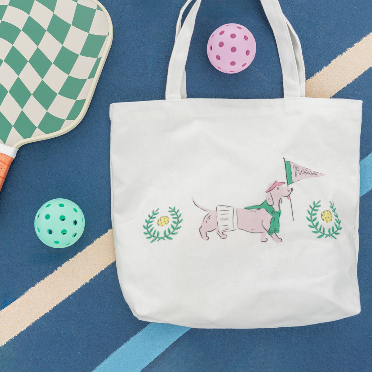 White tote bag with dog illustration on a blue background with sports equipment