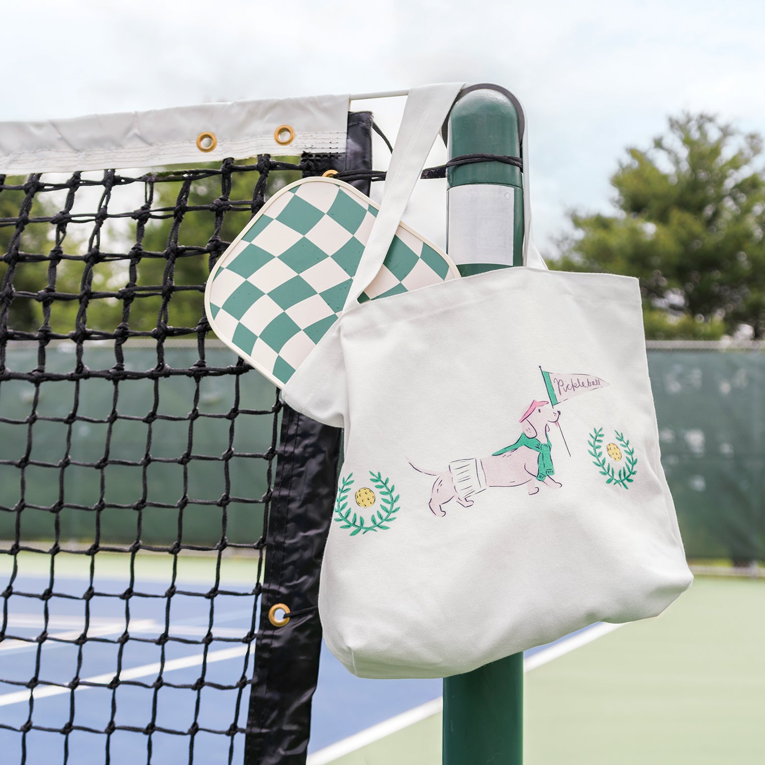 Tote bag with dog illustration hanging on a tennis net