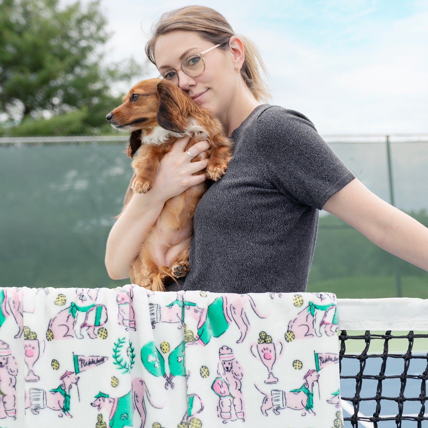 Woman holding a small brown dog outdoors with a patterned fabric in the foreground.