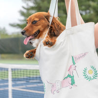 Dog sticking its head out of a tote bag with a dachshund illustration on a tennis court.