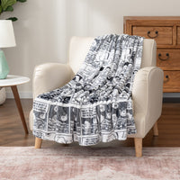 A white throw blanket with Peanuts comic strip illustrations draped over an armchair.