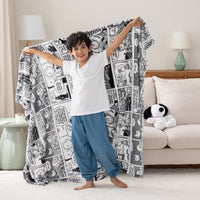 A child standing in a room, holding a black-and-white throw blanket with Peanuts comic strip illustrations.