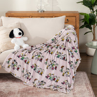 Lilac colored peanuts character throw draped over the arm of a grey chair with a snoopy plushy next to it.