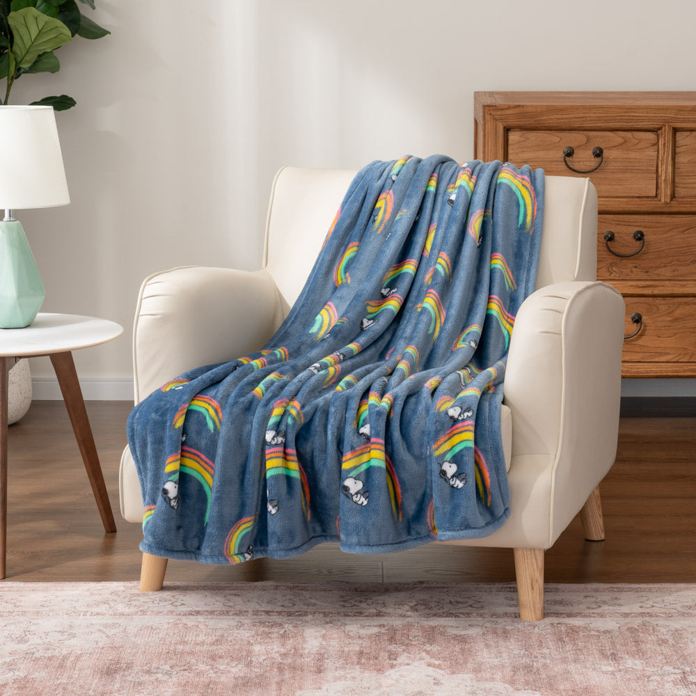 A blue throw blanket with Snoopy on a rainbow draped over an armchair.
