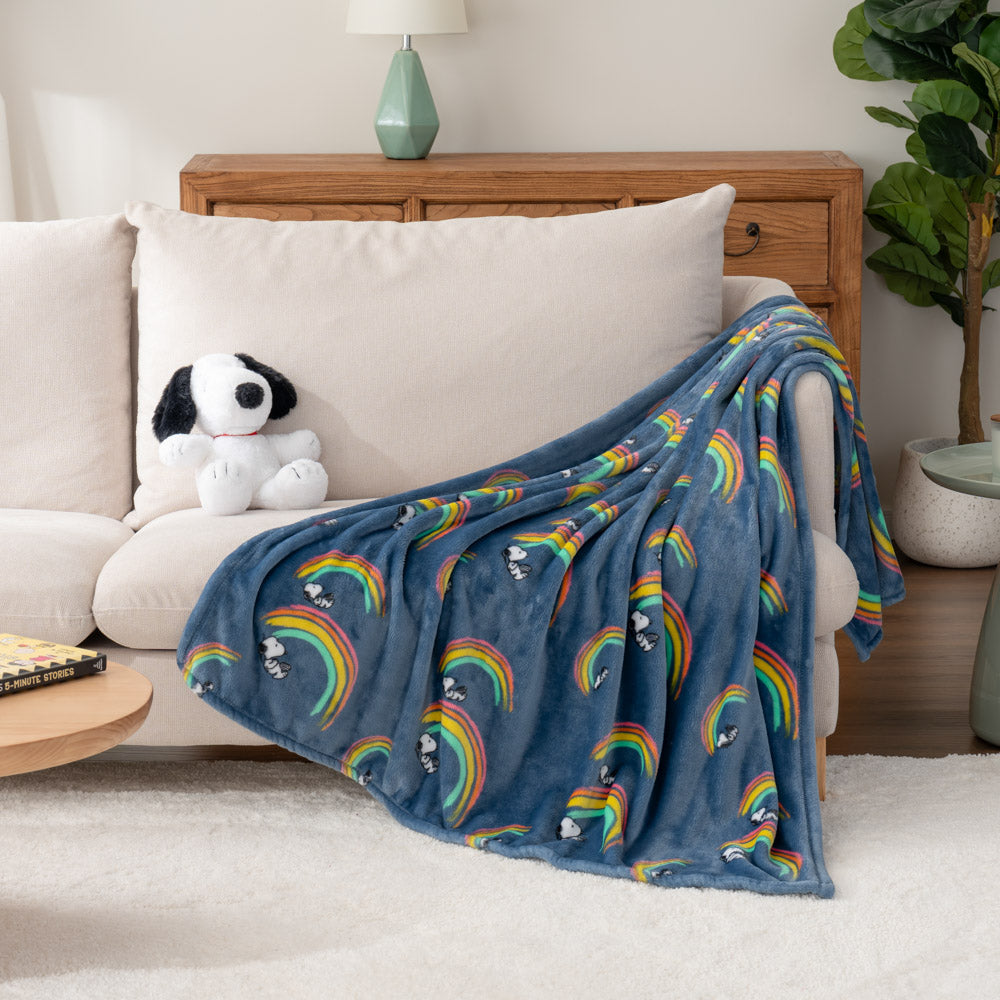 A blue throw blanket with Snoopy on a rainbow draped over an armchair.