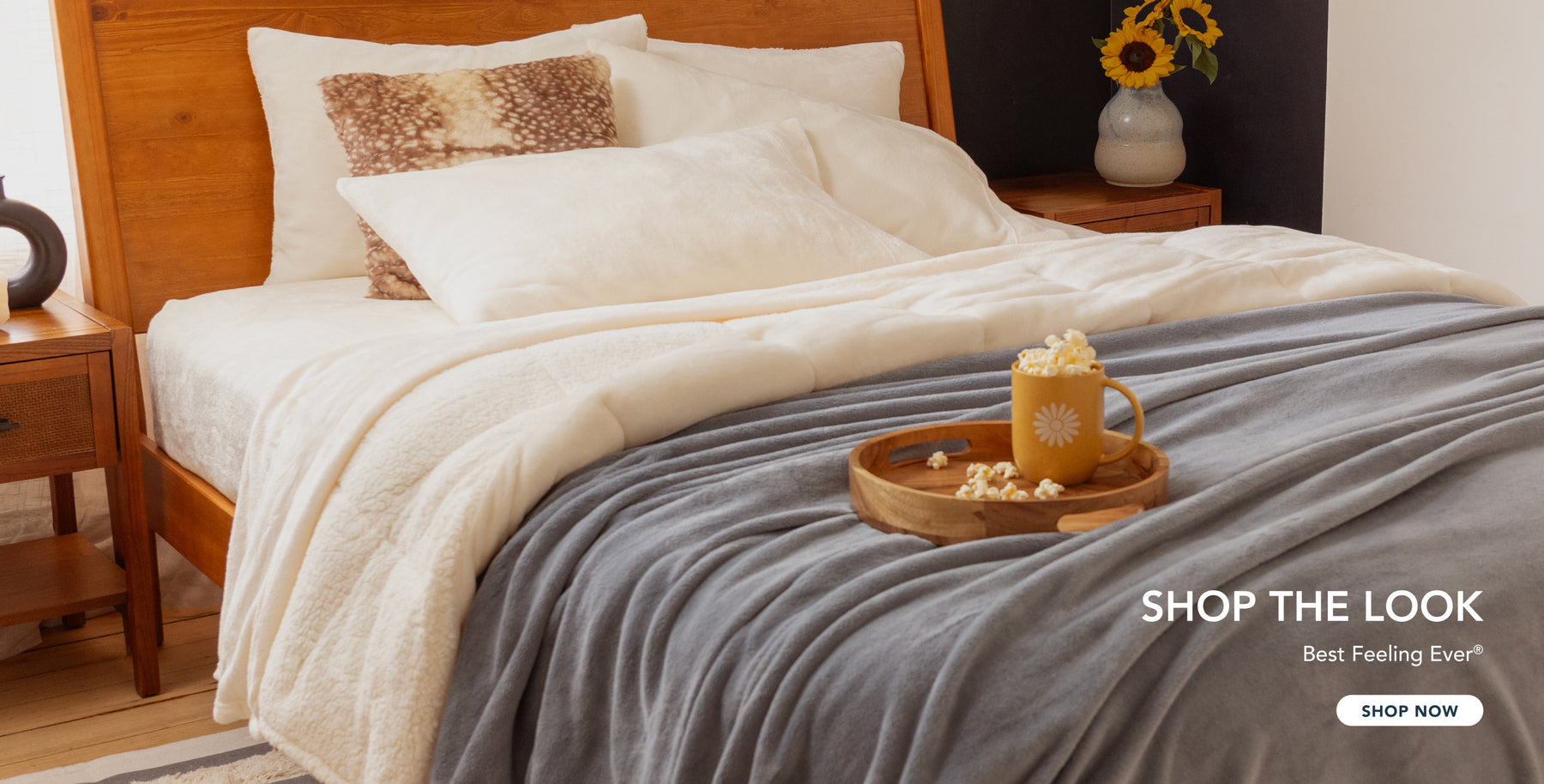 Image of a bedroom styled with cream sheets and a comforter, plush a light blue blanket, popcorn, and sunflowers.