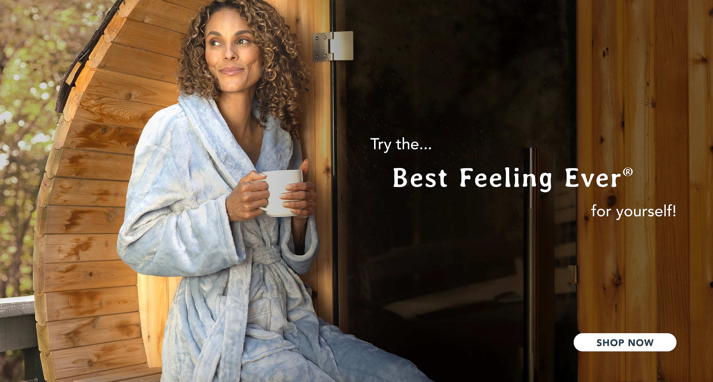 A woman standing outside of a sauna with a mug in hand wearing a blue VelvetLoft Robe with the memo "Try the best feeling ever for yourself".